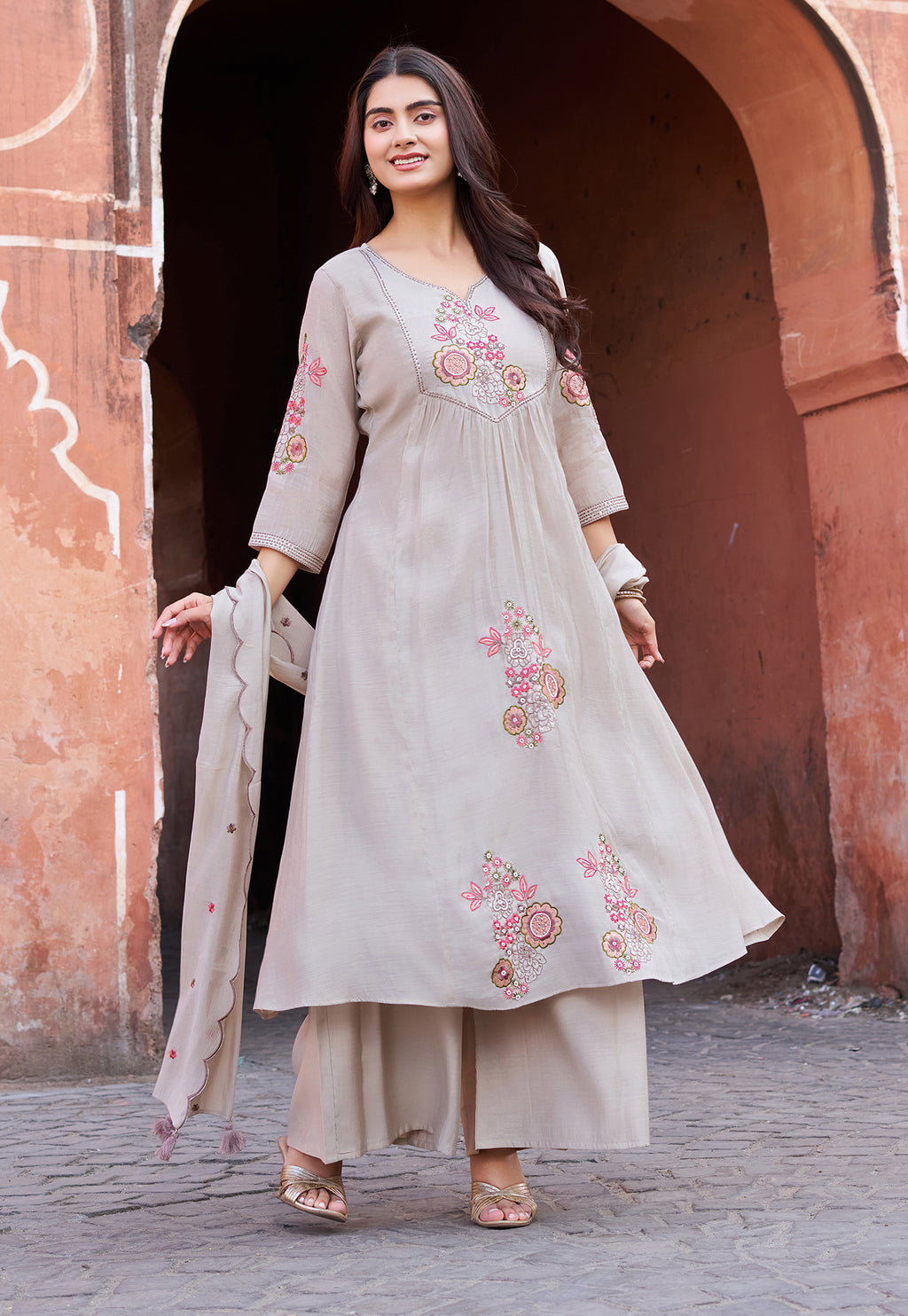 Woman in a traditional outfit with floral embroidery standing in front of an archway.