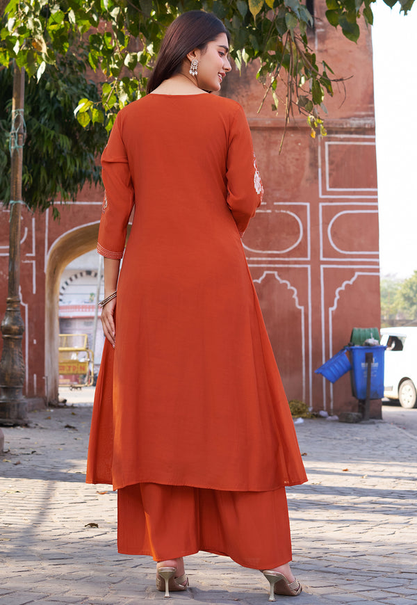 Woman in an orange outfit standing in front of a red building with white arches.
