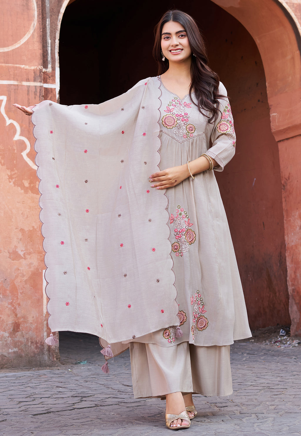 Woman in a traditional outfit with embroidery standing in front of an archway.