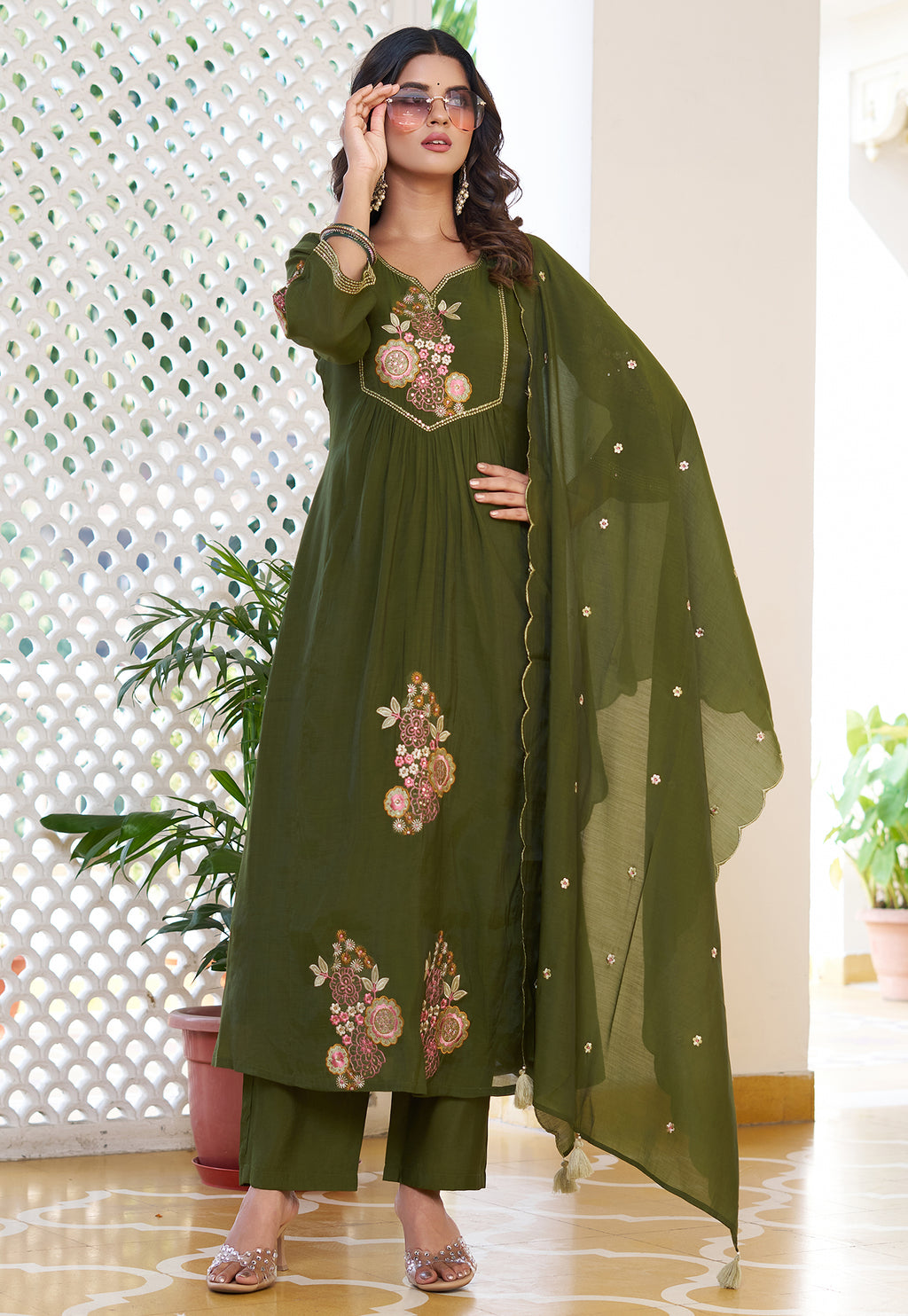Woman wearing a green embroidered outfit with a dupatta in an indoor setting.