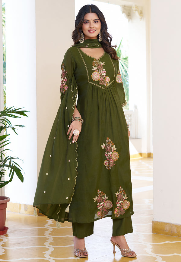 Woman wearing a green embroidered traditional outfit in a bright room.