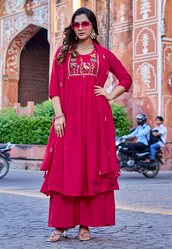 Woman in a red traditional outfit with embroidery standing in front of an architectural building.