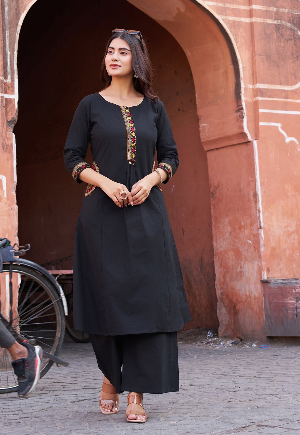 Woman in a black traditional outfit standing in front of a red sandstone archway.