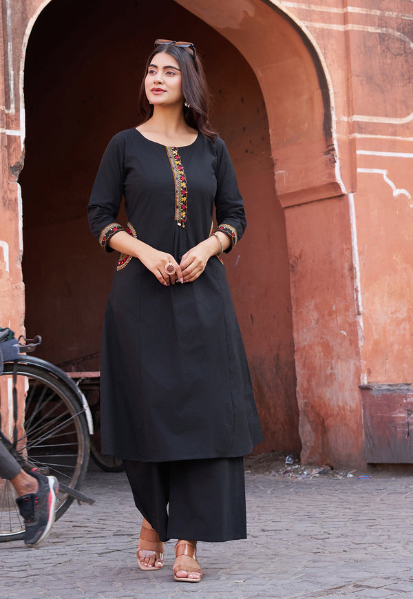Woman in a black traditional outfit standing in front of a red sandstone archway.