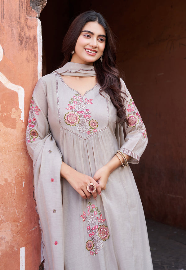 Woman wearing a light gray embroidered dress standing against a textured wall.