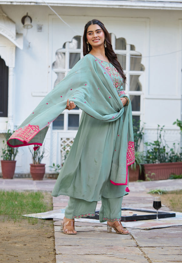 A woman models a mint green ethnic salwar kameez suit with a matching dupatta draped over her shoulders, set against a white building background.