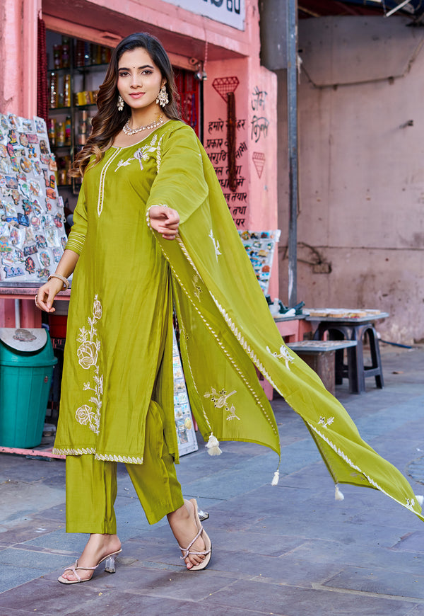 A woman models a lime green ethnic salwar kameez suit with white floral embroidery, featuring a matching dupatta, in an outdoor street setting.