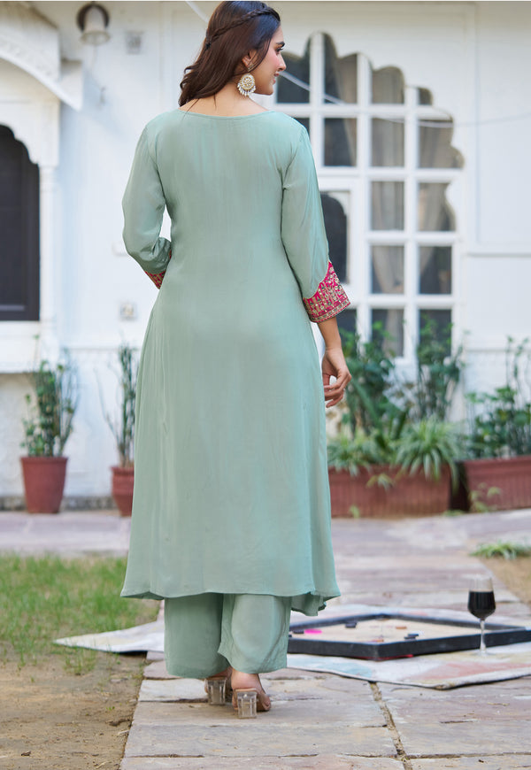 A woman wearing a sage green three-piece kurta set with matching pants, shown from the back in an outdoor courtyard setting.